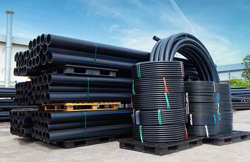 Stacked black corrugated pipes on pallets outdoors